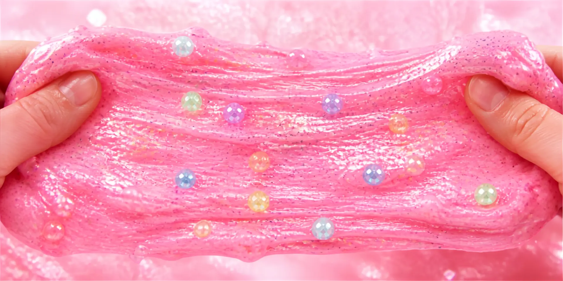 Hands stretching pink glitter slime with colorful beads